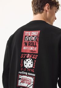 Sort langærmet t-shirt med røde og hvide grafiske tryk, herunder tekst og terningemotiver, med et vintage Rolling Stones-design.