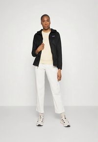 Μαύρο ελαφρύ μπουφάν με κουκούλα, μπεζ πουλόβερ, λευκό παντελόνι και ουδέτερα αθλητικά παπούτσια. Απλός σχεδιασμός με casual εφαρμογή και καθαρές γραμμές.