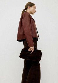 Giacca cropped in pelle marrone, pantaloni scuri marrone a gamba dritta, che tiene una clutch in suede marrone scuro. Design minimalista con linee pulite.