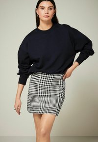 Sweatshirt oversize bleu marine associé à une mini-jupe ajustée en vichy noir et blanc. La tenue présente un design décontracté et des tissus texturés.