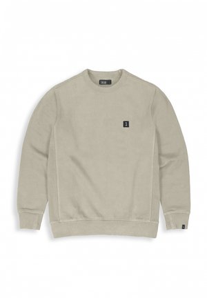 Beige sweatshirt with long sleeves, round neck, and ribbed cuffs. Features a small logo patch on the chest. Soft fabric texture.