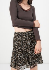 Brun långärmad topp med en rundad halsringning och kontrasterande kant, kombinerad med en svängig svart kjol med ett mångfärgat abstrakt mönster.