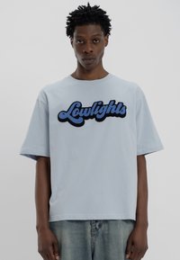 Ανοιχτό μπλε βαμβακερό t-shirt με υπερμεγέθη εφαρμογή, στρογγυλή λαιμόκοψη, κοντά μανίκια και κεντημένο λογότυπο "Lowlights" σε σκούρο και ανοιχτό μπλε.