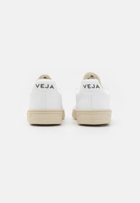 Hvide sneakers med en glat læderoverdel og beige gummisåler. Har "VEJA" branding bagpå med kontrasterende sort skrift.