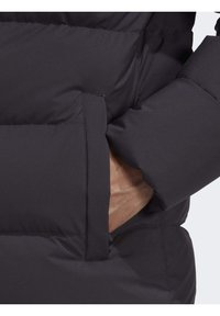 Schwarze gepolsterte Jacke mit einer Seitentasche mit Klappe, die eine glatte Textur und strapazierfähigen Stoff zeigt, mit sichtbaren Nähdetails.