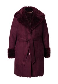 Burgundyröd kappa tillverkad av mjuk mocka med en fluffig krage och manschetter, med bälte i midjan och knappstängning. Slät textur och knälängd.