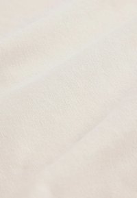 Gros plan sur un tissu tricoté beige clair et doux avec de subtiles plis diagonaux et une texture fine et lisse.