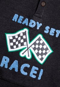 Dunkelgrauer Stoff mit gesticktem Text "READY SET RACE" in Hellblau und zwei Schachbrettflaggen, umrandet in Weiß und Grün.