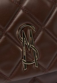 Braune Lederhandtasche mit gestepptem Muster, ausgestattet mit goldfarbenen Logo-Hardware und kontrastierenden Nähten.
