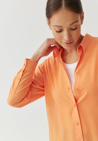 Button-up shirt in bright orange, featuring a collar, long sleeves, smooth texture, and button accents on cuffs and placket.