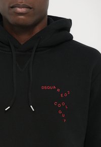 Sort hættebluse med snoretræk og sølv aglets. Har en rød tekstlogo-design "DSQUARED2 COOL GUY" arrangeret diagonalt på fronten.