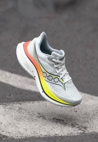 Lightweight running shoe in white mesh with gray accents. Features a bright orange and yellow gradient on the sole and perforated detailing.