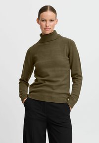 Olivgrön polotröja i mjukt stickat material, med en figurnära design, ribbade muddar och nederkant. Bärs tillsammans med svarta byxor.