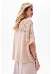 Lichtbeige oversized gebreide top met een textuur van bladerenpatroon, korte mouwen en een losse pasvorm, gecombineerd met neutraalgekleurde broeken.