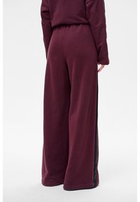 Szerokie spodnie w kolorze wina, wykonane z miękkiego materiału, z teksturowanym bocznym panelem i elastycznym paskiem w talii dla komfortu.