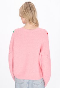 Rosa, übergroßer Strickpullover mit strukturiertem Finish, der offene Strickdetails und kontrastierende Farbakzente an den Schultern aufweist.