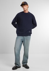 Maglione a costine blu navy con colletto rotondo, abbinato a jeans a gamba dritta blu chiaro e scarpe nere, con un dettaglio logo ricamato.