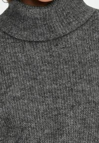 Gros plan sur un pull à col roulé gris en tricot montrant la texture et le détail côtelé du col.