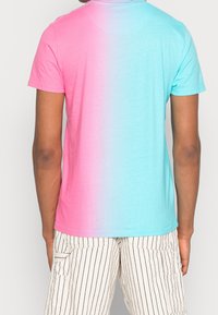 Person som bär en t-shirt med kort ärm i en vertikal rosa till blå gradient och vita shorts med svarta vertikala ränder.