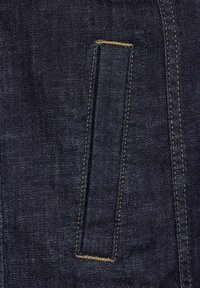 Tmavě modrá džínovina s obdélníkovou kapsou s kontrastním béžovým prošíváním, která se vyznačuje hladkým povrchem a klasickými designovými prvky.