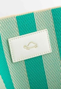 Tela de rayas en turquesa y crema con un acabado texturizado, que presenta una etiqueta de cuero blanco con un logo de tortuga dorado en relieve.
