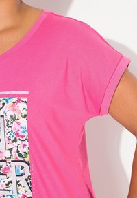 Růžové tričko s krátkým rukávem s květinovým vzorem a stříbrným nápisem na přední straně, vyrobené z měkké tkaniny s uvolněným střihem.