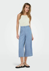 Top de punto beige claro sin mangas combinado con culottes de mezclilla de pierna ancha y cintura alta. La modelo lleva sandalias planas negras con tiras ligeras.