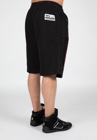 Black textured shorts with a loose fit, featuring side pockets and a label. Paired with black high-top sneakers.