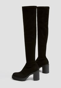 Botas negras por encima de la rodilla en suave ante, con un tacón grueso, punta redonda y suela texturizada para agarre y estabilidad.