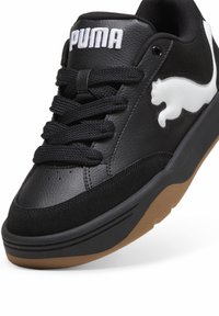 Baskets noires avec une tige en cuir texturé, arborant un logo Puma blanc, des lacets noirs et une semelle en caoutchouc naturel. Détails en finition lisse et suédée.