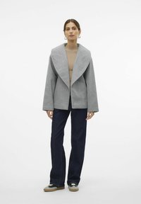 Grå ullblandingsjakke med bred, notch-kollare, oversized design, kombinert med mørkeblå jeans og joggesko. Glatt tekstur, uformell stil.