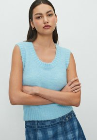 Top senza maniche di maglia azzurro chiaro con scollatura a coste e orlo inferiore, caratterizzato da una morbida e pelosa trama. Il modello lo abbina a una gonna a quadri.