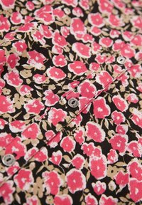 Bloemige shirtstof met levendige roze en beige bloemen op een zwarte achtergrond, voorzien van een zichtbare knoop voor het sluiten.