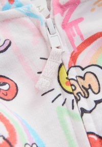 Reißverschluss-Hoodie mit einem weißen Stoffbasis und bunten Cartoon-Mustern, darunter rot, gelb und grün Akzenten. Texturierter Zipper.