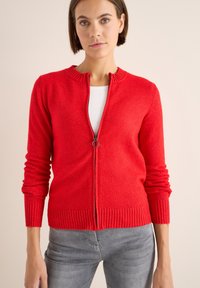 Cardigan rosso con zip realizzato in tessuto a maglia testurizzato, dotato di un colletto e polsini a coste e una chiusura con zip liscia.