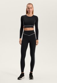 Fekete sportos, hosszú ujjú crop top fehér csíkozással és barna részletekkel. Magas derekú, fekete leggingssel, fehér csíkokkal párosítva.