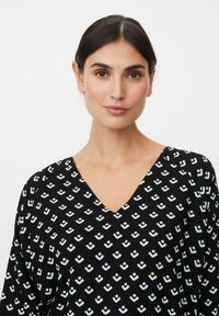 Zwarte top met een V-halsontwerp en een herhalend geometrisch patroon van lichtblauwe en gele vormen. Zachte, vloeiende stoftextuur.