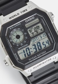 Montre numérique Casio avec un bracelet noir, des accents argentés, un écran LED affichant l'heure, une carte du monde, et des fonctionnalités telles que les alarmes et la résistance à l'eau.