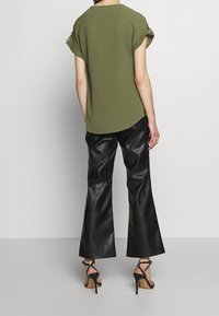 Top de manga corta verde oliva con mangas enrolladas, combinado con pantalones acampanados de imitación cuero negro y sandalias de tacón alto negras con tiras.