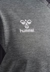 Szara koszulka sportowa z dekoltem w serek i czarnymi akcentami, z białym logo "hummel" oraz emblematem pszczoły z przodu. Teksturowana tkanina.