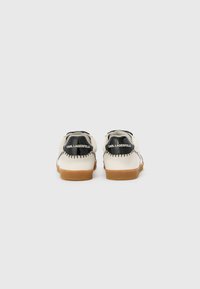 Leather sneakers featuring a cream upper, black heel accents, contrasting stitching, and a brown rubber sole. Rear logo displays "KARL LAGERFELD."