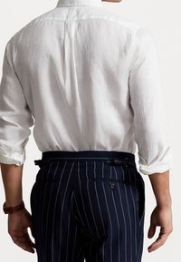 White linen shirt with rolled sleeves paired with dark blue pinstriped trousers featuring belt loops and back pockets.