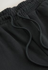 Sorte sweatpants med ribbet elastisk talje og snore. Stoffet er blødt, tekstureret og har en glat overflade.