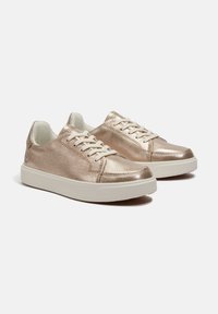 Metallic rose gold sneakers with a smooth surface, white laces, and a thick white sole; features a rounded toe and minimalistic design.