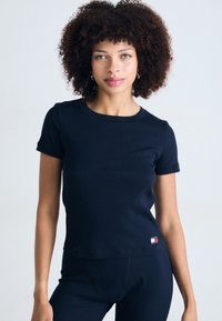 Navy blue ribbed T-shirt with short sleeves, round neckline, and a small logo tag at the hem. Fitted design with smooth texture.