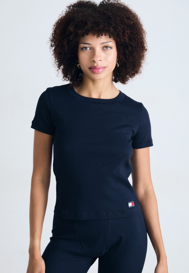 Navy blue ribbed T-shirt with short sleeves, round neckline, and a small logo tag at the hem. Fitted design with smooth texture.