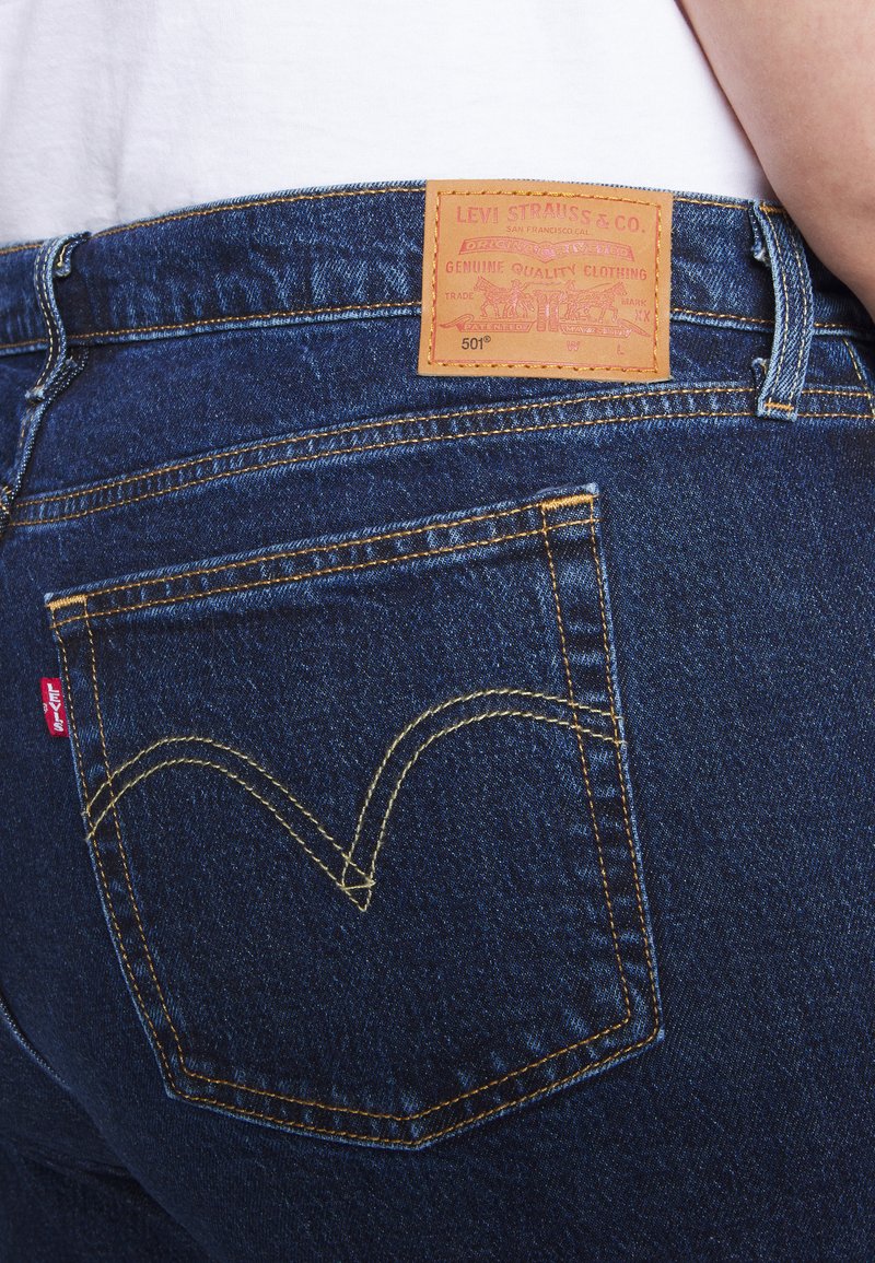 Dunkelblaue Denim-Jeans mit einer auffälligen Gesäßtasche, die ein rotes Levi's-Label trägt. Ein brauner Lederpatch zeigt 'Levi Strauss & Co.' und '501.'