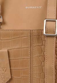 Tan leren tas met krokodillenstructuur, zilveren hardware en gestikte accenten. Logo "BURKELY" in zilver gebosseleerd.