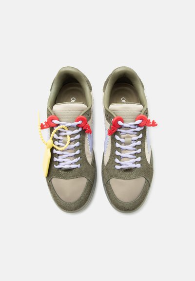 Ζευγάρι αθλητικά παπούτσια σε ελαιώδες πράσινο και μπεζ με λευκά κορδόνια, κόκκινα κλιπ κορδονιών και κίτρινη ετικέτα στο αριστερό παπούτσι.