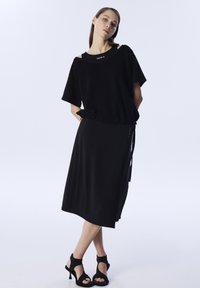 Zwarte oversized top met korte mouwen en een ronde halslijn, gecombineerd met een zwarte rok tot op de knie. Beide kledingstukken hebben een gladde textuur.